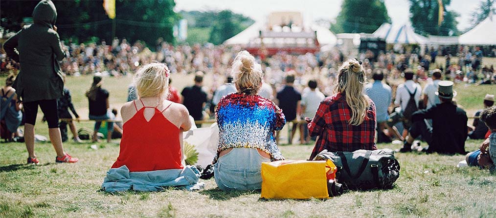Grupo de chicas sentadas en el cesped en frente del escenario de un festival
